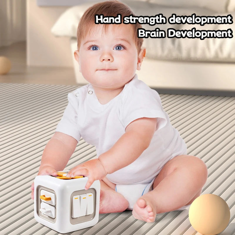 A baby in a white onesie is sitting on a striped mat, playing with a tactile cube toy. Text highlights "Hand strength development, Brain Development."