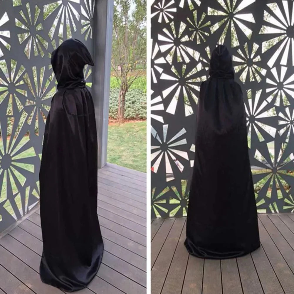 A person in a black cloak stands in front of a decorative metal screen with geometric cutouts. The background shows grass and trees, viewed from the side and back.