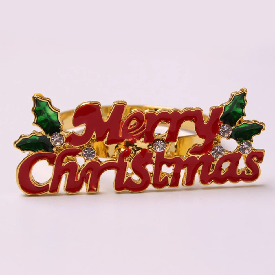 Festive brooch with "Merry Christmas" in red letters, adorned with green holly leaves and sparkling gems, set on a gold background.