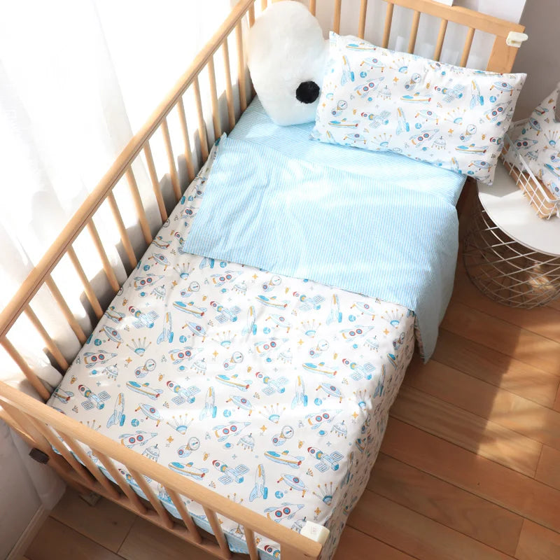 A wooden crib with space-themed bedding, featuring rockets and planets. A blue striped blanket and matching pillow, alongside a plush toy, complete the cozy setup by the window.
