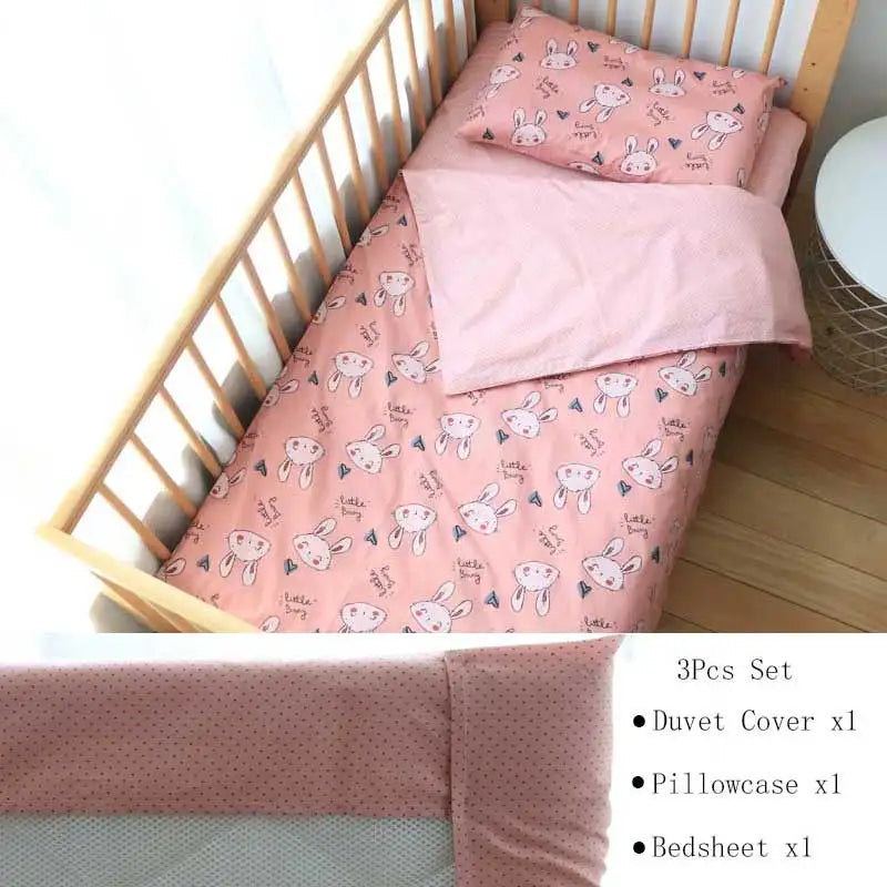 Crib bedding set with a pink duvet cover, pillowcase, and bedsheet featuring a cute bunny pattern. Includes a side table next to the crib. Text: "3Pcs Set: Duvet Cover x1, Pillowcase x1, Bedsheet x1."