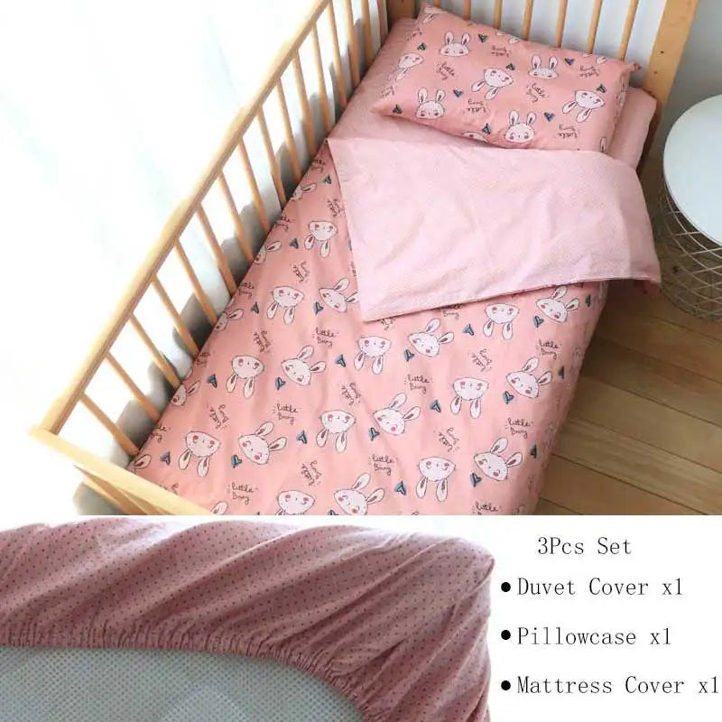 Pink children's bed set with a bunny pattern. Includes a duvet cover, pillowcase, and mattress cover. Set displayed on a wooden crib beside a small white table.