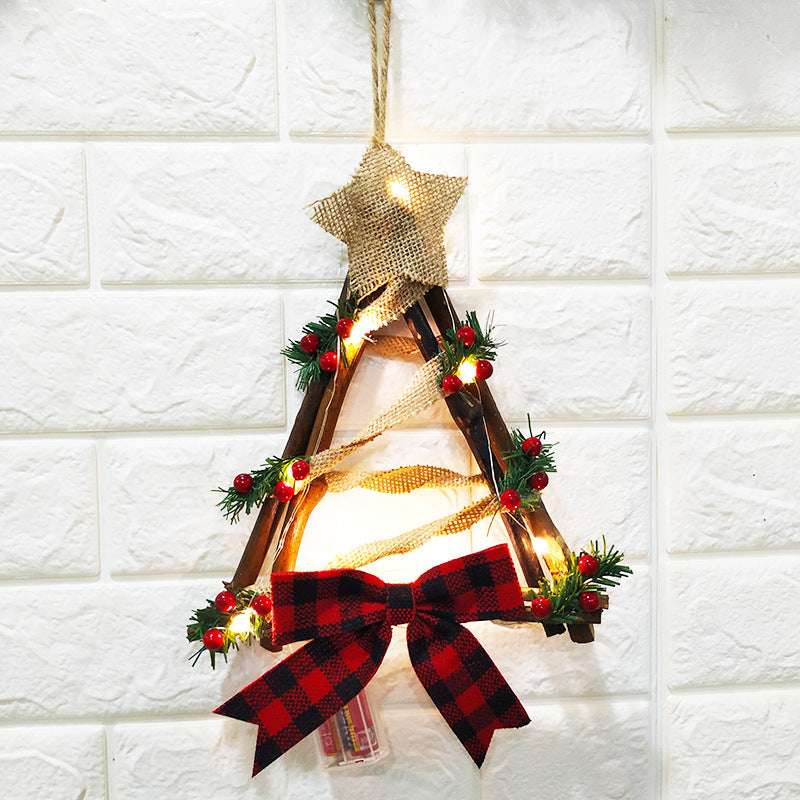 Rustic Christmas tree wall hanging with burlap star, twigs, red berries, pine sprigs, and checkered bow, adorned with warm fairy lights on a white textured background.