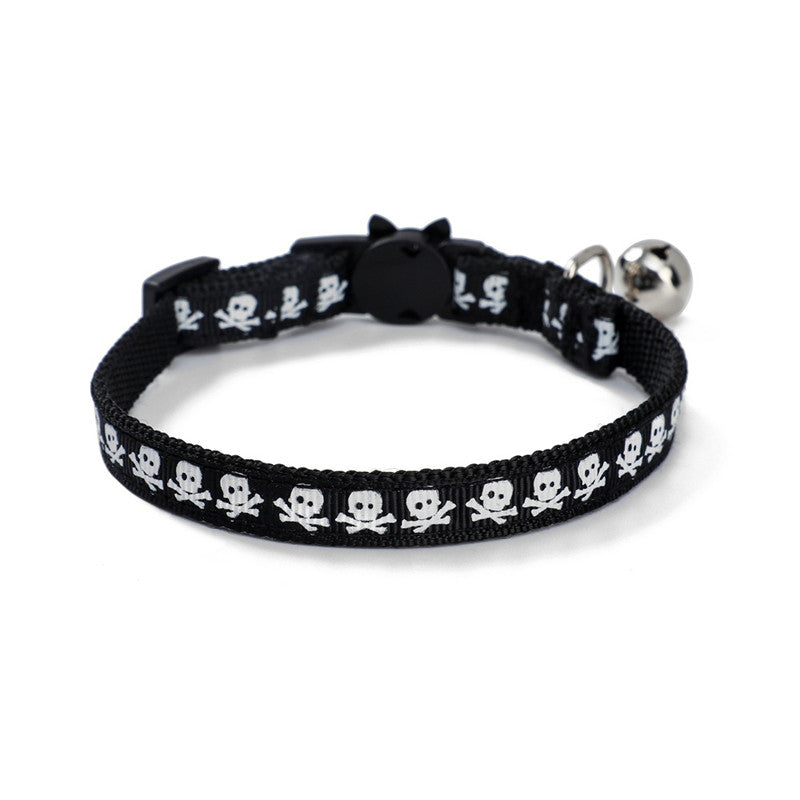 Black pet collar with white skull and crossbones pattern, featuring a small silver bell and a black plastic clasp, set against a white background.