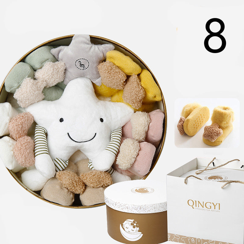 Gift box with a smiling star plush, assorted colorful socks, a pair of yellow baby booties, and a white gift bag labeled "QINGYI."