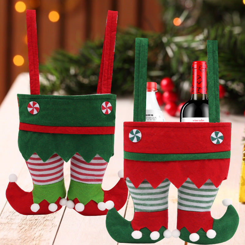 Festive wine bottle holders resembling elf legs, made of red and green felt with candy button details. One holder contains bottles, set against a blurred Christmas background.