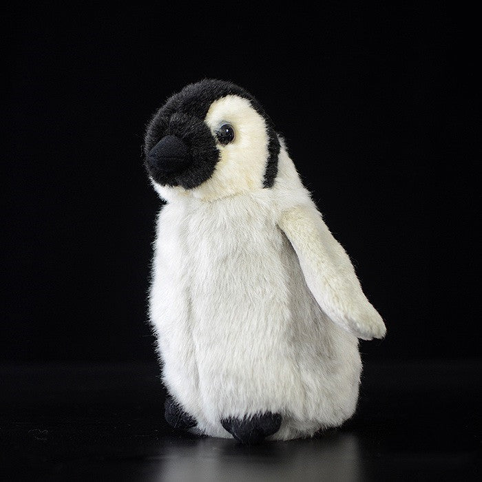 A fluffy penguin plush toy with a black face, white and gray body stands on a black background. Its wings are slightly open, and the expression is soft and endearing.