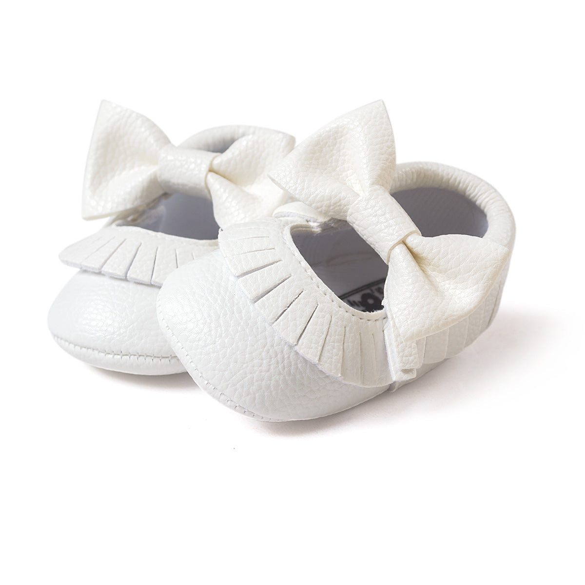 White baby shoes made of textured material, featuring large bows and fringe detailing. The design is elegant and suitable for special occasions or casual wear.