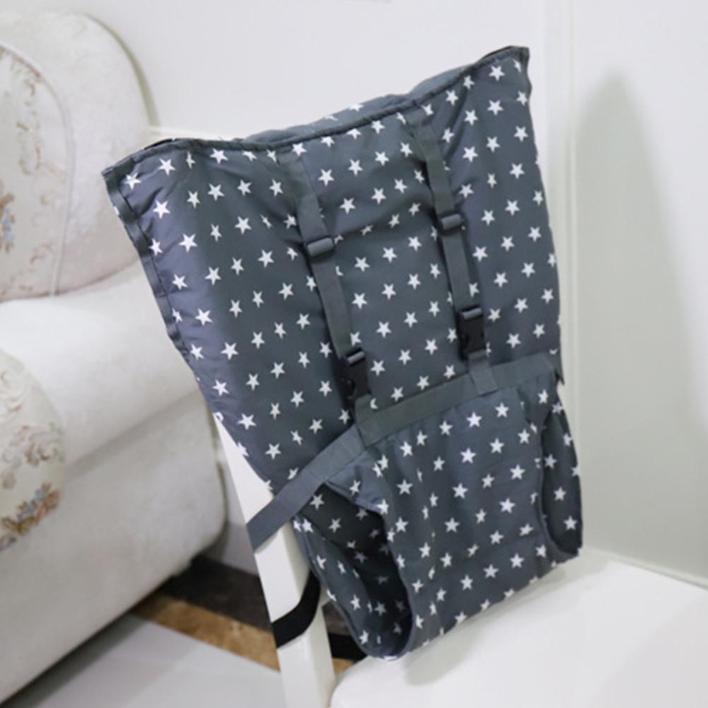 Star-patterned gray baby carrier draped over a white chair, next to a floral-patterned couch in a living room setting.