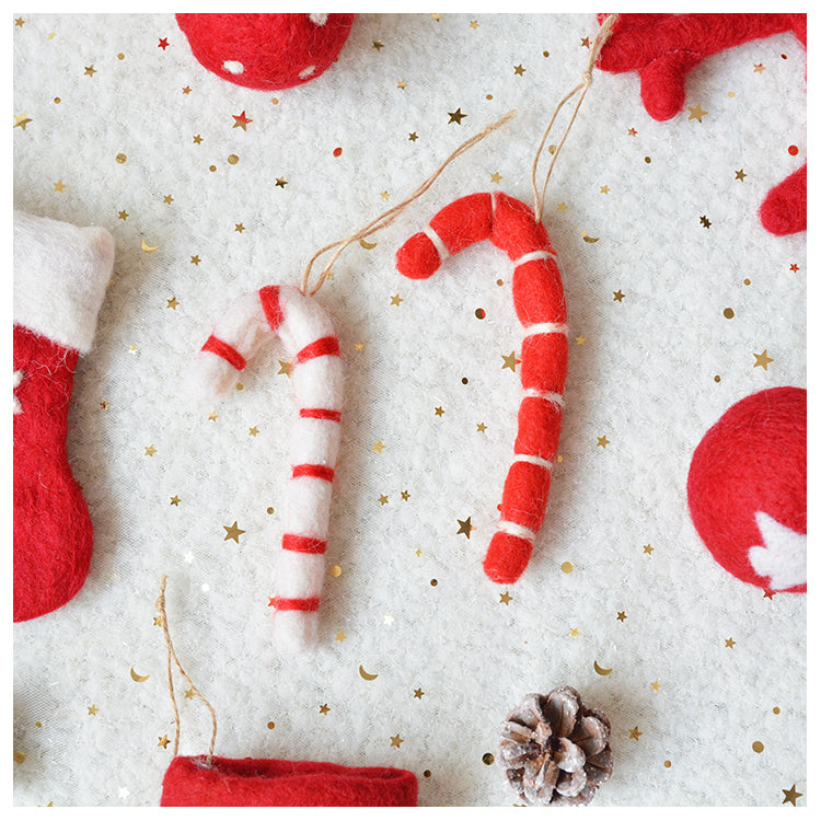 Felt Christmas decorations on white, star-patterned fabric: red and white candy canes, red stocking, pinecone, and red baubles with a festive theme.