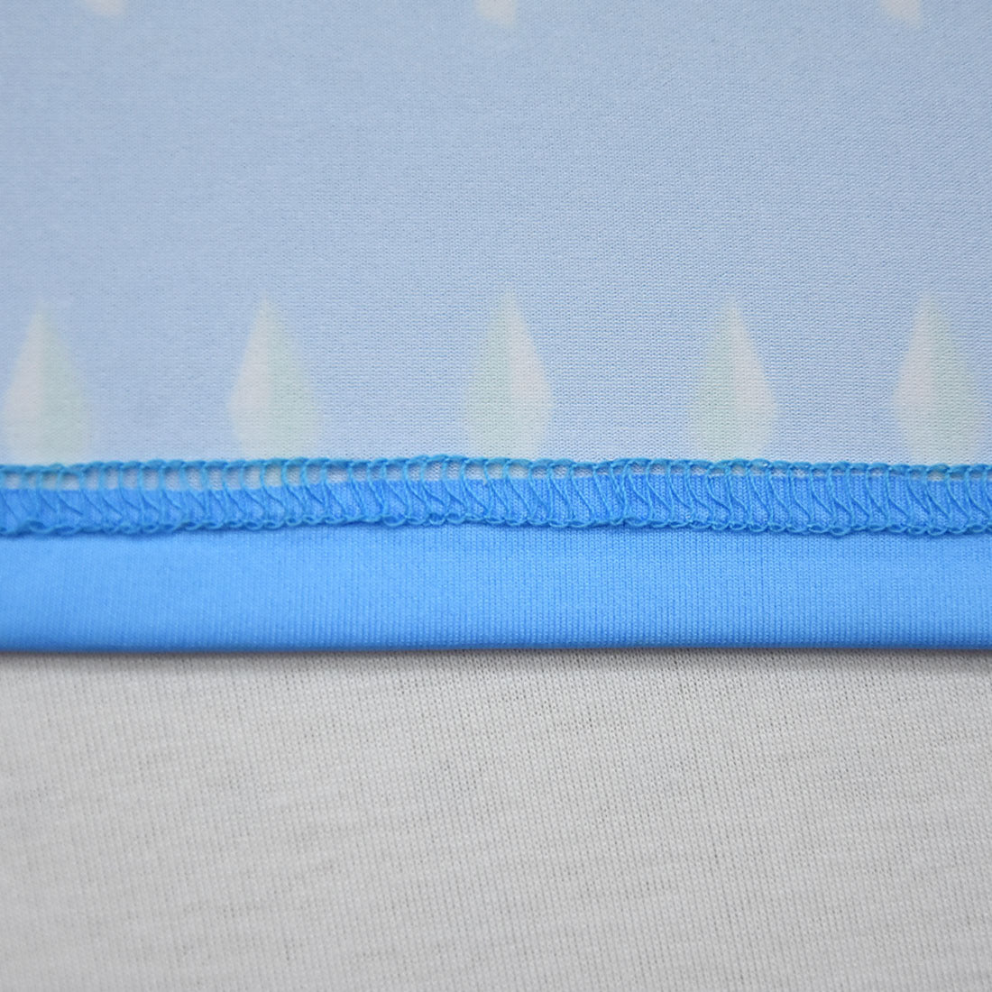 Close-up of a light blue fabric with a zigzag stitched seam and a smooth hem. The fabric has a subtle geometric pattern, and the seam contrasts against a white background.