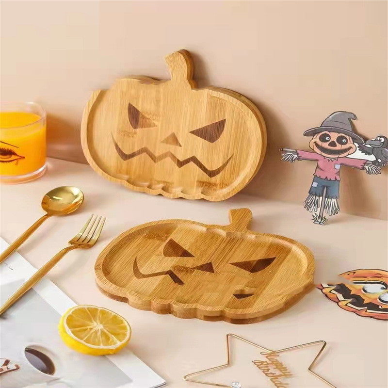 Bamboo pumpkin-shaped trays with carved jack-o'-lantern faces on a table. Nearby are a glass of orange juice, a scarecrow cutout, gold utensils, lemon slices, and a star decoration.