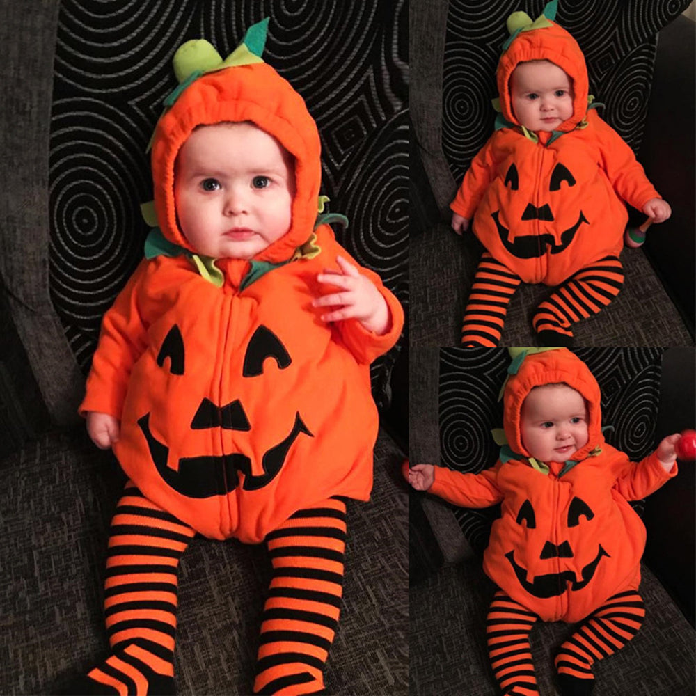 Baby in a pumpkin costume with green leaves and stem on the hood, sitting on a dark patterned fabric. The outfit has a jack-o'-lantern face, paired with striped leggings.