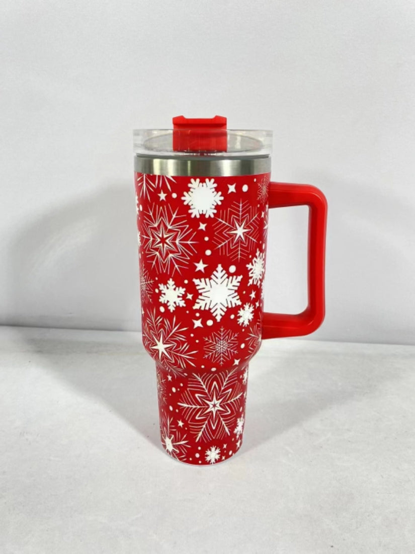 Red travel mug with white snowflake patterns, featuring a large handle and a clear lid. The mug sits on a plain white surface against a light gray background.