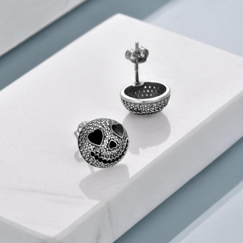 Silver pumpkin-shaped earrings with black eyes and smile, textured surface, displayed on a white platform against a minimal background, casting soft shadows.
