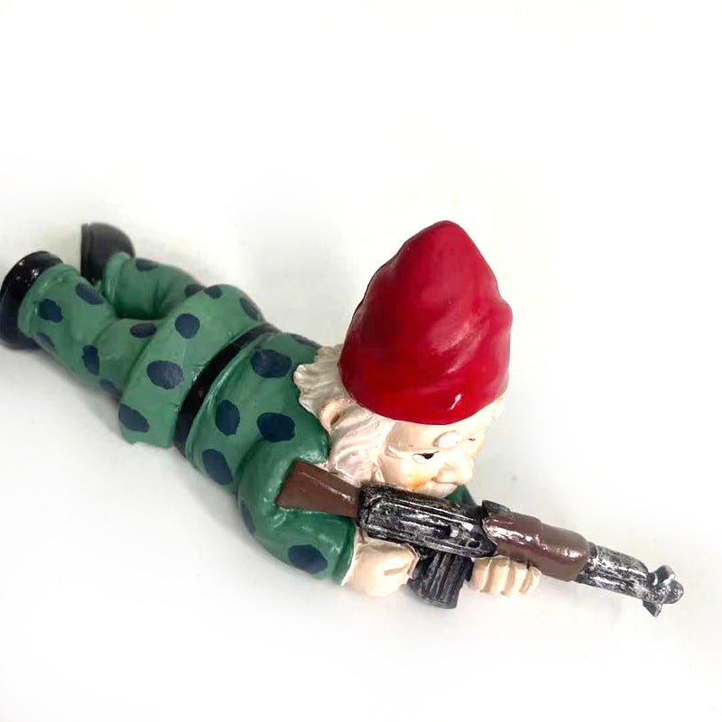 A garden gnome lies prone on the ground, wearing a red hat and green outfit with polka dots, aiming a rifle playfully.