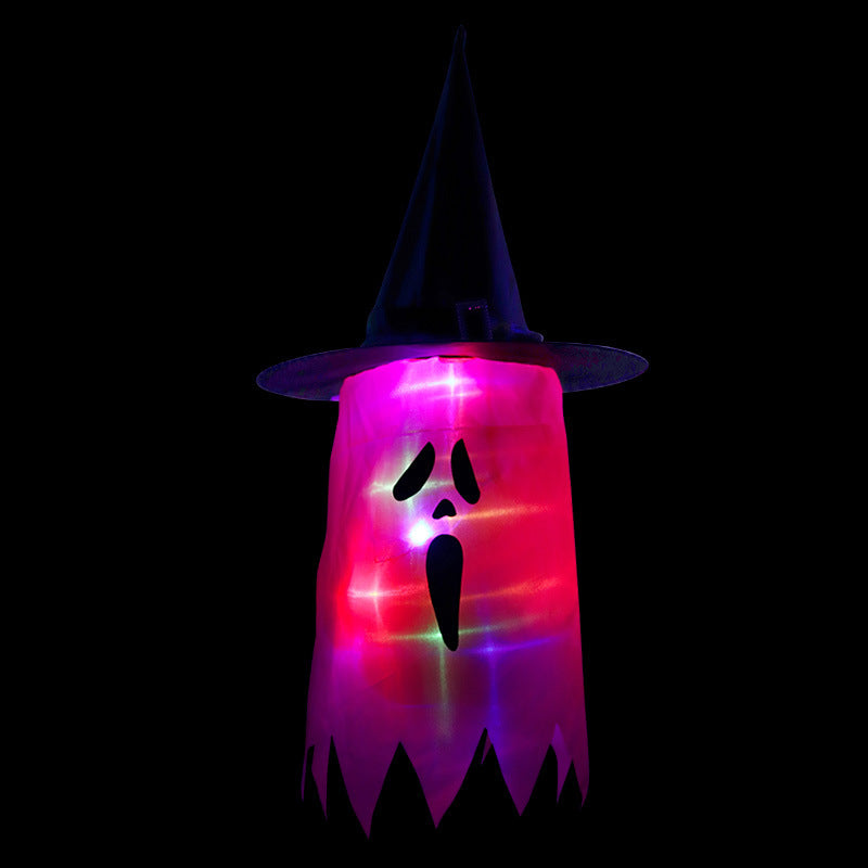 Illuminated ghost decoration with a witch hat, glowing in red and purple hues. The ghost has expressive black eyes and a mouth, set against a dark background.