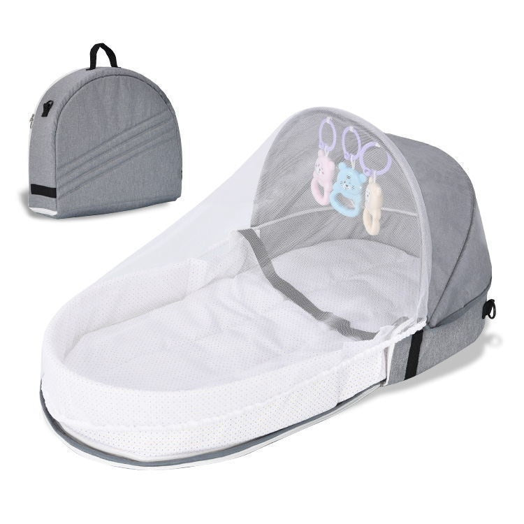 Portable baby bassinet with a grey canopy, white netting, and attached toys. Includes a matching grey carrying bag with a handle, showcasing its foldable travel-friendly design.
