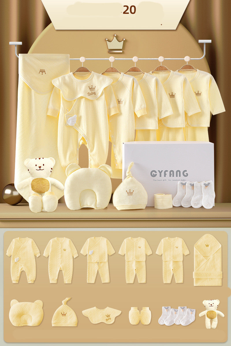 Yellow baby clothing set with rompers, tops, hat, mittens, bib, socks, blanket, teddy bear, and a neck pillow, displayed with a gift box on a beige backdrop.