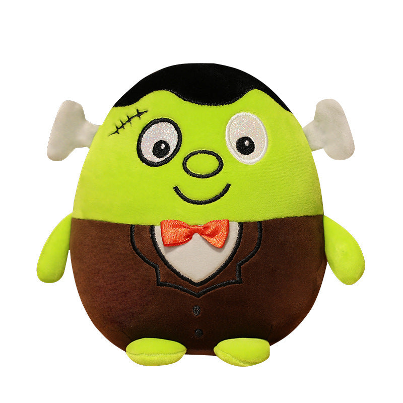 Cute, plush toy resembling a green Frankenstein monster with stitched details, large round eyes, a wide smile, and an orange bow tie. It wears a brown suit with black accents.