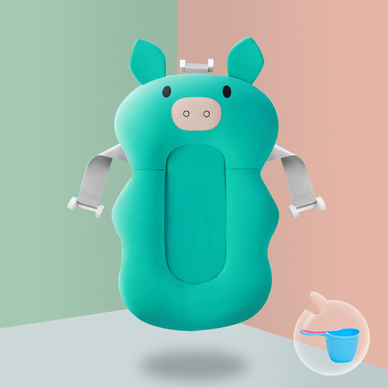 A green infant bath seat shaped like a pig, with ears and face, is equipped with adjustable straps. A small image inset shows a blue cup and pink spoon. Background is pastel green and pink.