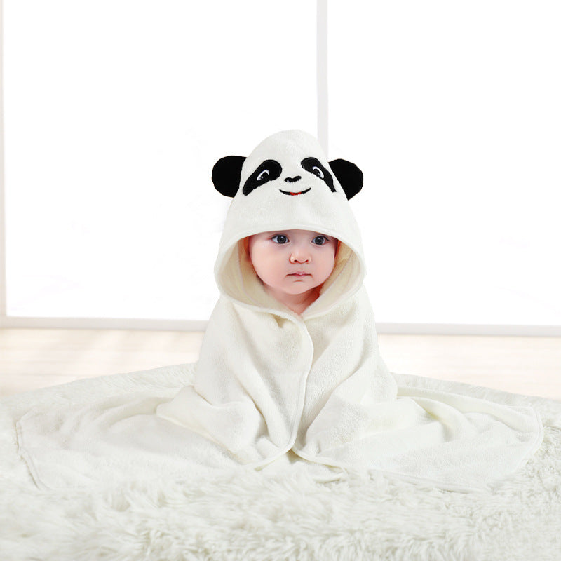 A baby sits on a fluffy white rug, wrapped in a panda-themed hooded towel with black ears and a smiling face design, looking curiously at the camera.