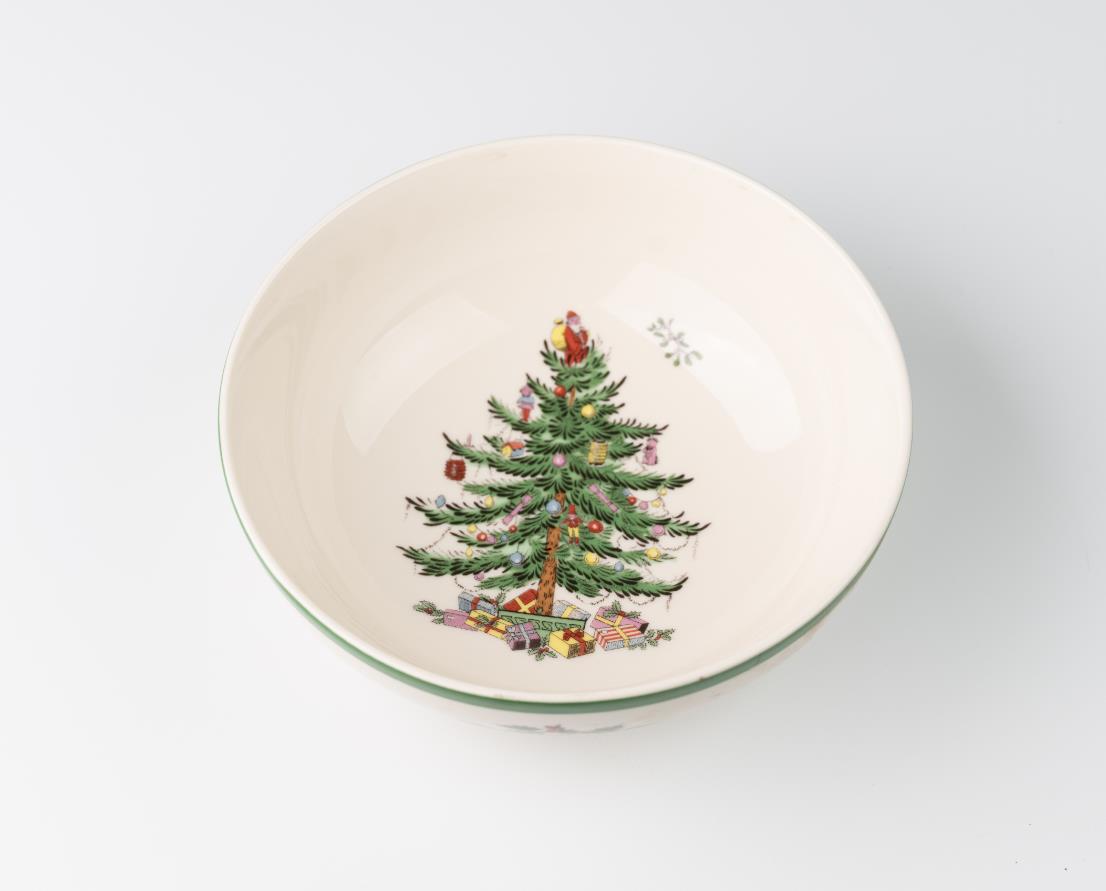 A cream-colored ceramic bowl with a Christmas tree design, featuring green branches, colorful ornaments, and presents underneath, centered inside the bowl.