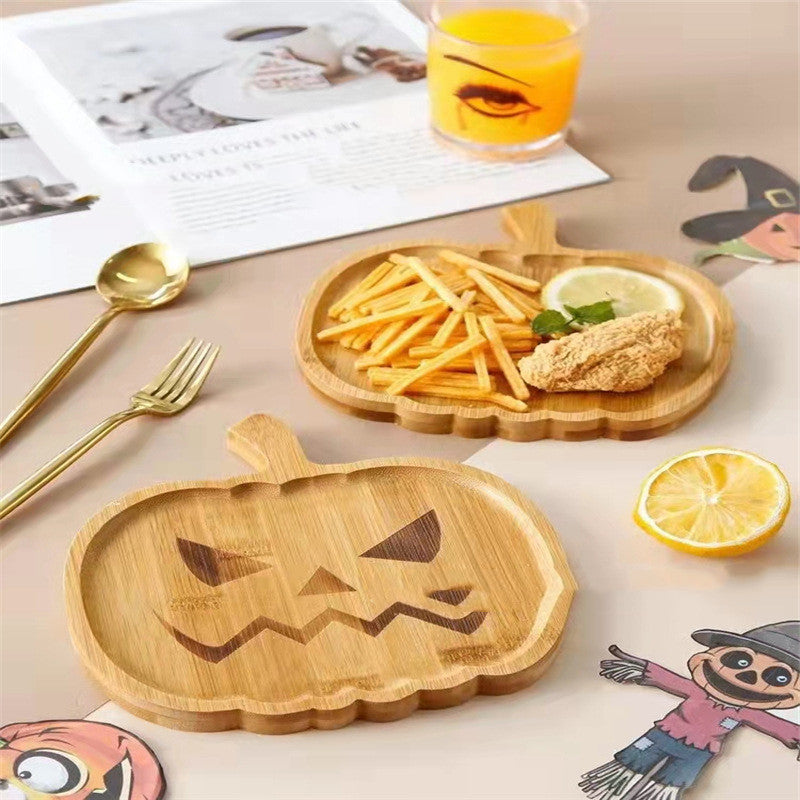 Pumpkin-shaped wooden plates with jack-o'-lantern designs hold fries and fried chicken. A glass of orange juice, gold cutlery, and autumn-themed decor complete the setting.