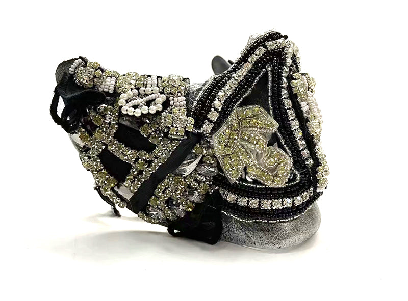 Intricately designed mask featuring black and silver beads, pearls, and crystals forming elaborate patterns, with metallic accents, displayed against a white background.