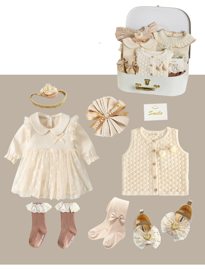 Baby clothing set with a cream dress, knitted vest, socks, and soft shoes featuring bows. Accessories include a crown headband and a bow, displayed with a suitcase.