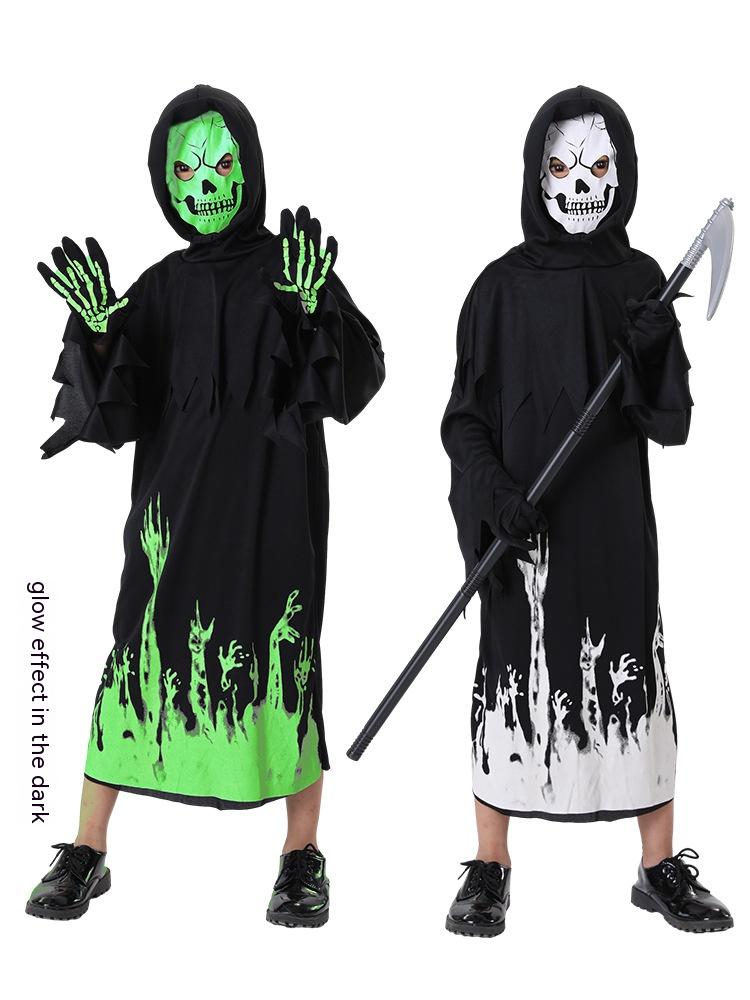 Two children in hooded Halloween costumes with glow-in-the-dark designs. One has a green skull mask and green hands, the other a white skull mask and holds a scythe.
