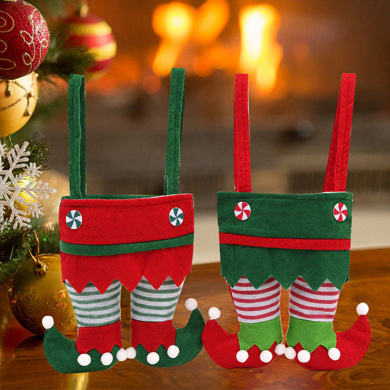 Two decorative elf-themed stockings, resembling elf pants with striped legs and curled shoes, hang by a fireplace. A Christmas tree with ornaments is partially visible.