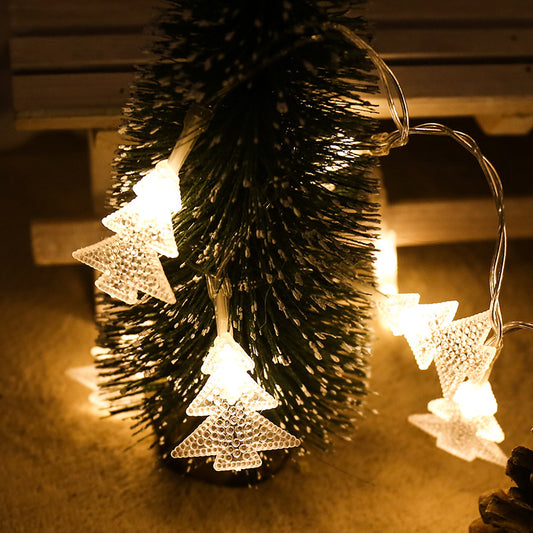 Small Christmas tree adorned with glowing, tree-shaped string lights, creating a warm, festive ambiance. Background shows a wooden surface partially illuminated.