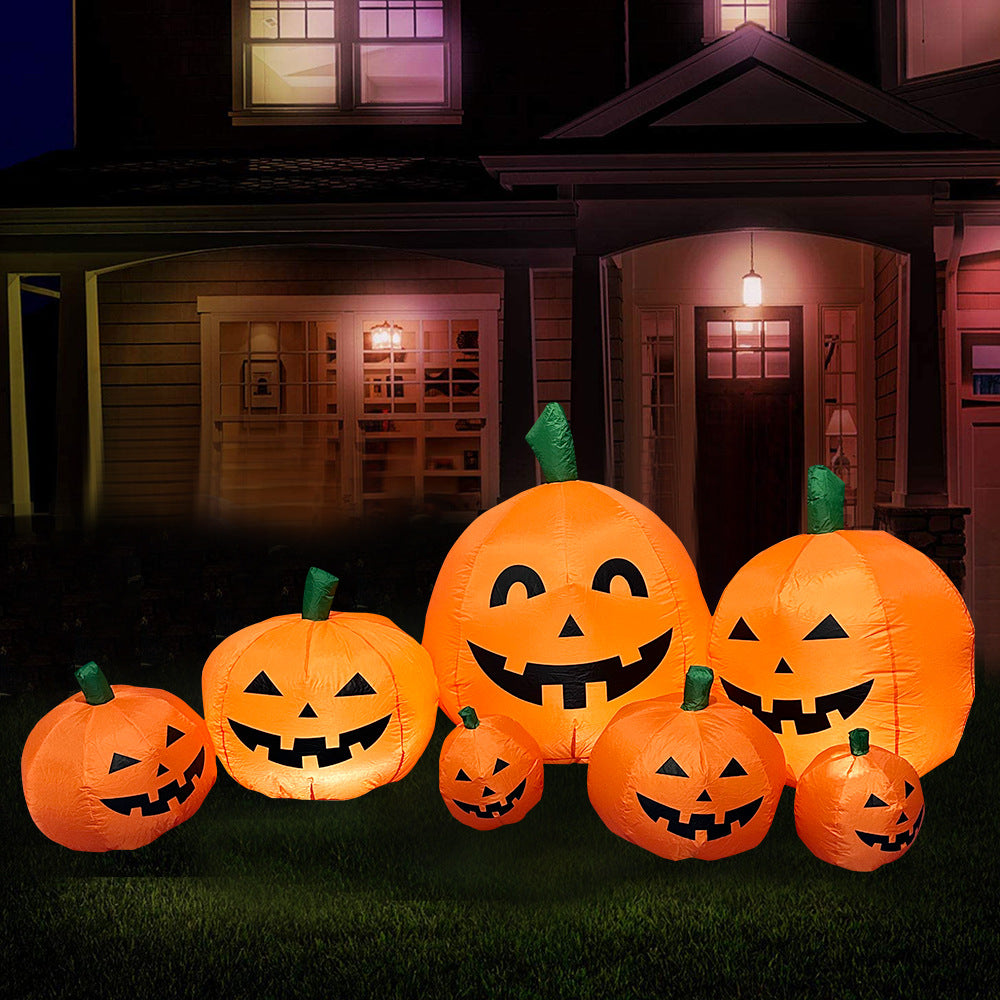 Inflatable jack-o'-lanterns of various sizes on a lawn, glowing at night. A house is in the background with warm lights coming from the windows and porch.