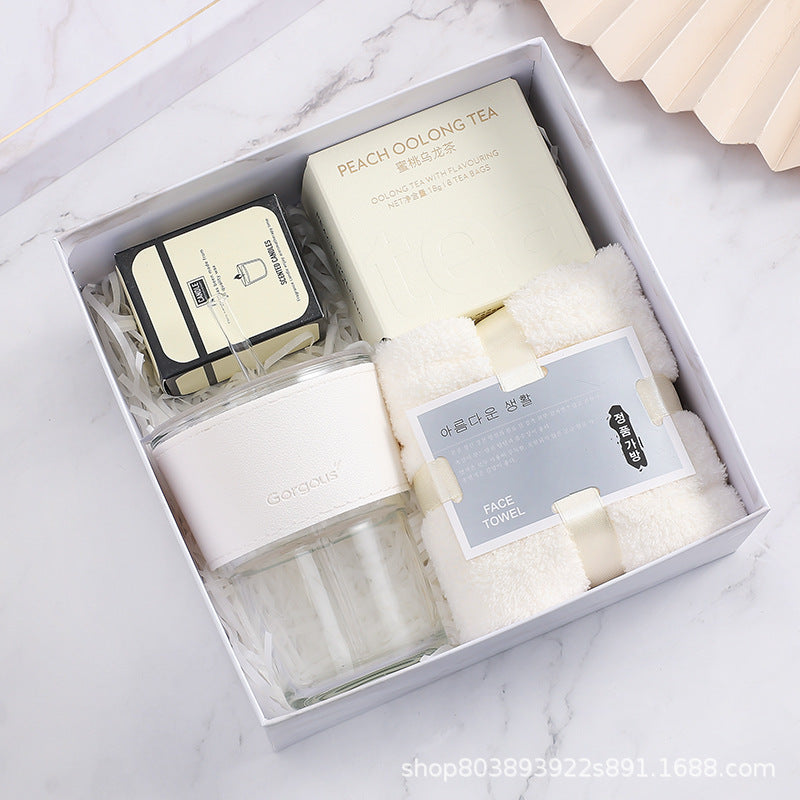 Gift box with a jar, peach oolong tea, black soap, and a white face towel arranged neatly on a bed of shredded paper, set against a marble background.