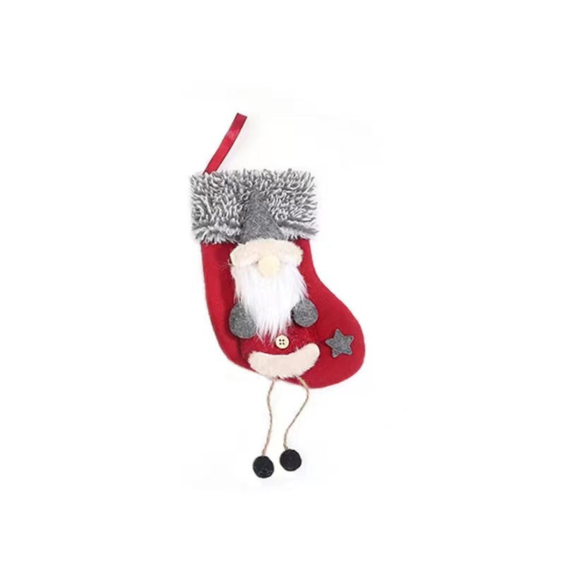 Red Christmas stocking with a plush gnome decoration, featuring a fluffy hat, white beard, and dangling legs with black shoes. A star and button detail are on the stocking.