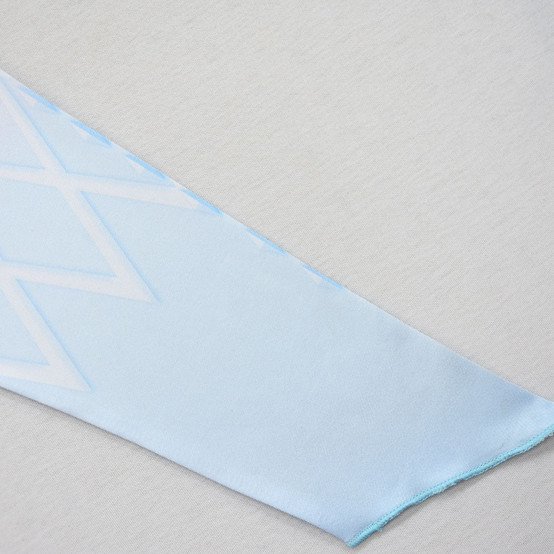 Close-up of a light blue fabric with a subtle geometric pattern on a light gray background, showcasing a stitched edge in the foreground.