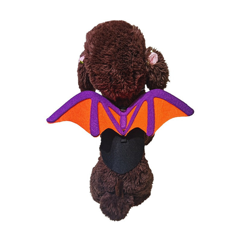 Fluffy brown dog plush wearing vibrant orange and purple bat wings. The plush is facing forward, showcasing floral accents behind its ears against a white background.