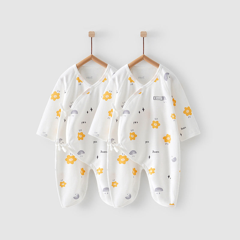 Two white baby onesies with yellow flowers, gray patterns, and text, hanging on wooden hangers against a light gray background.
