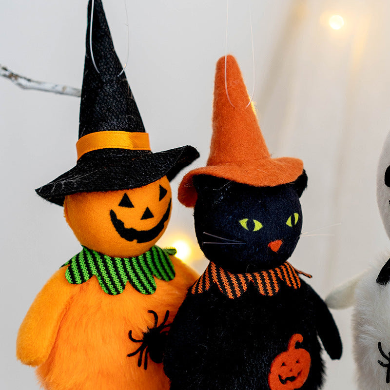 Two plush Halloween figures: an orange jack-o'-lantern with a black witch hat, and a black cat with an orange witch hat and pumpkin decoration. Background string lights.