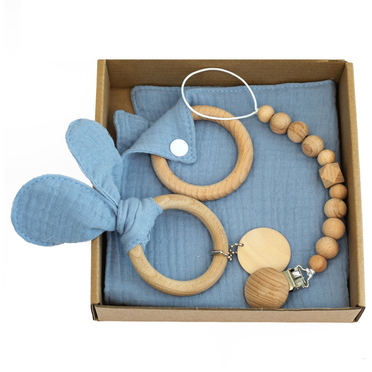 Box containing wooden teething rings and a pacifier clip with natural beads, set on a folded blue cloth with bunny ear detail.