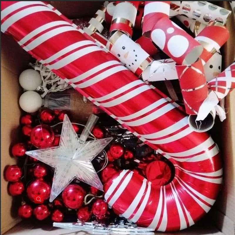 Box filled with Christmas decorations, including red and white striped candy canes, red baubles, white spheres, a silver star, and festive crackers.