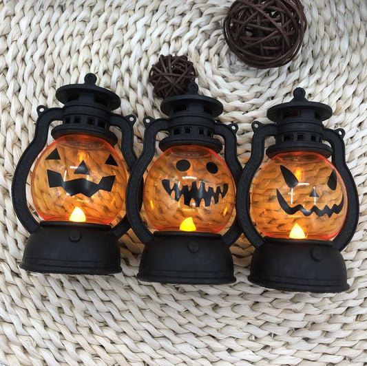 Three Halloween-themed lanterns with carved pumpkin faces glow with orange light. They are set on a woven surface, with decorative balls in the background.