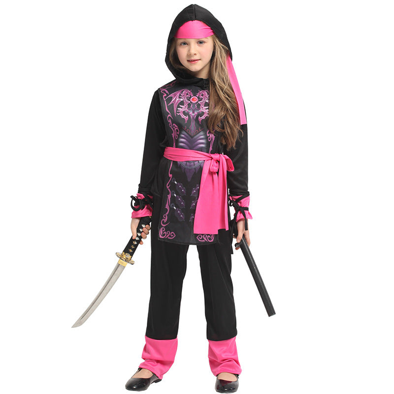 A child in a black and pink ninja costume holds a sword and nunchaku. The outfit features a pink sash, headband, and detailed chest design, paired with pink accents on the sleeves and pants.