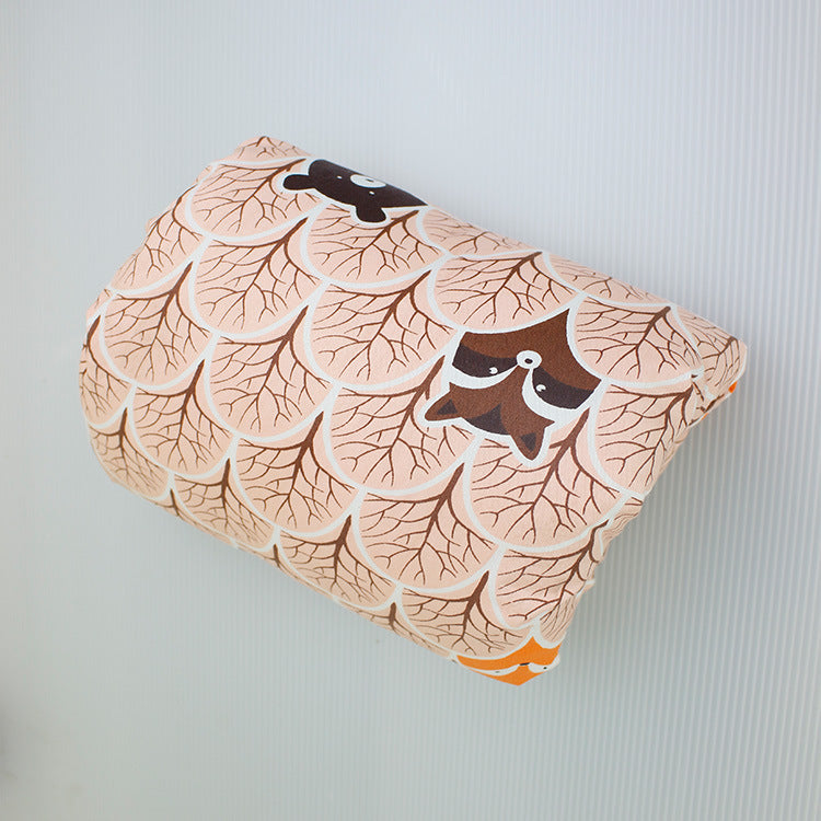 A cushion with a playful design featuring fish scales and animal faces, in tones of brown and peach, resting against a light, subtly textured background.
