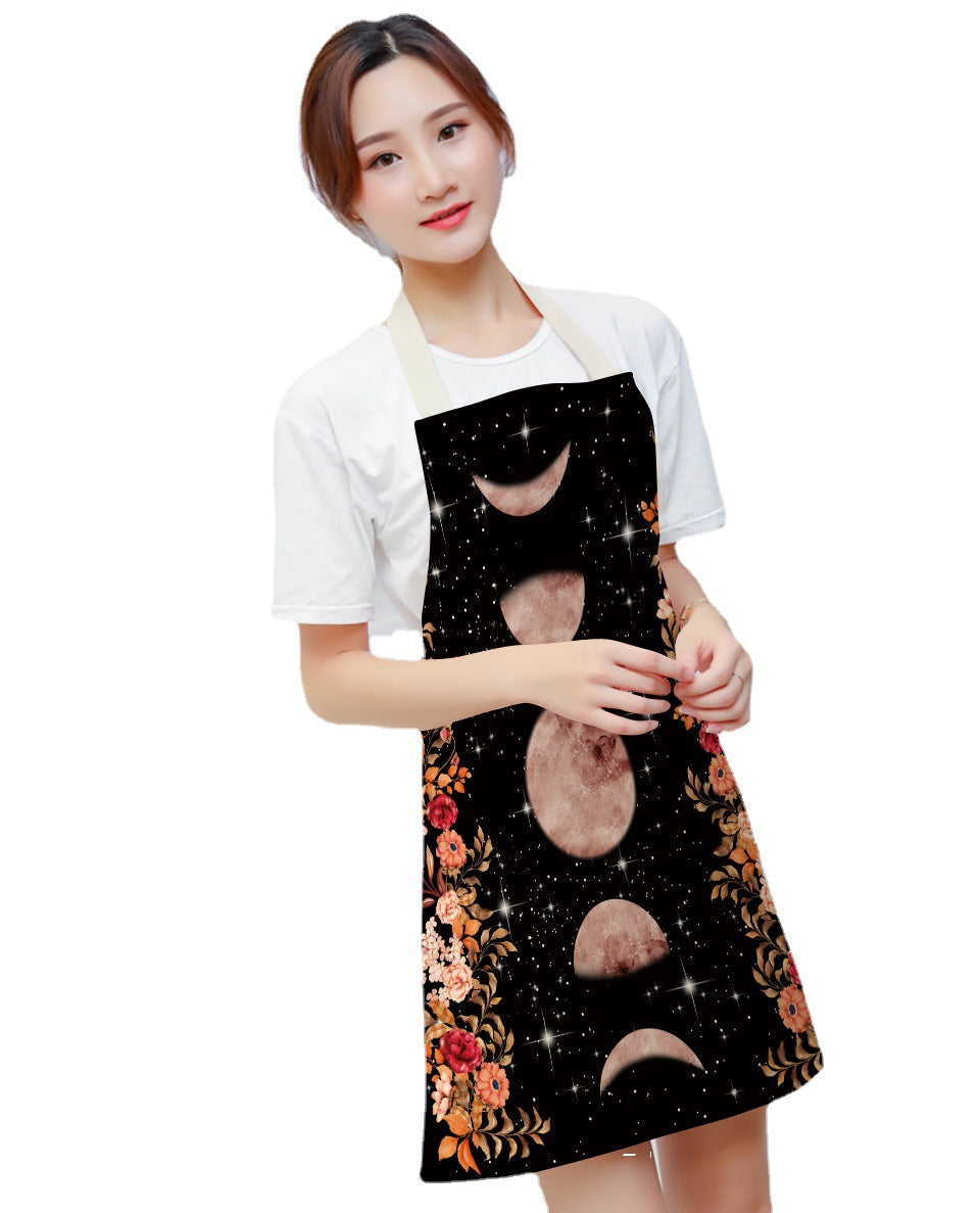 A person wearing a white shirt and an apron featuring moon phases and floral patterns against a starry background. The apron has a cosmic and artistic design.
