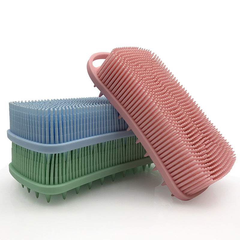 Stacked silicone pet grooming brushes in blue and pink with bristles and finger grip handles, resting on a white surface.