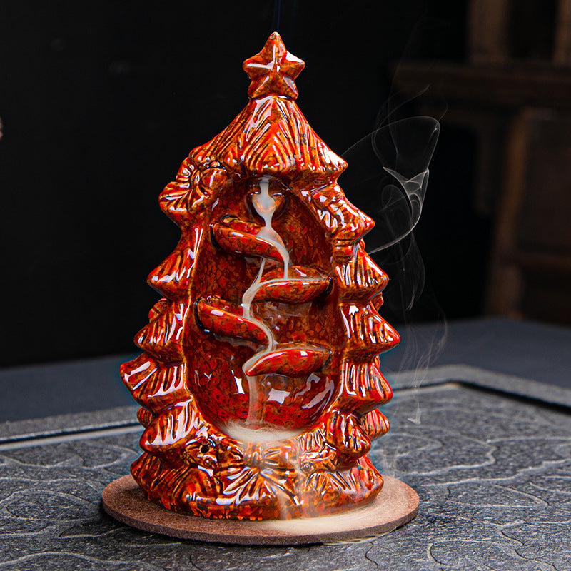 Ceramic incense holder shaped like a Christmas tree with cascading smoke. The red, glossy finish has a star on top and detailed branches. Smoke trails down in a spiral pattern.