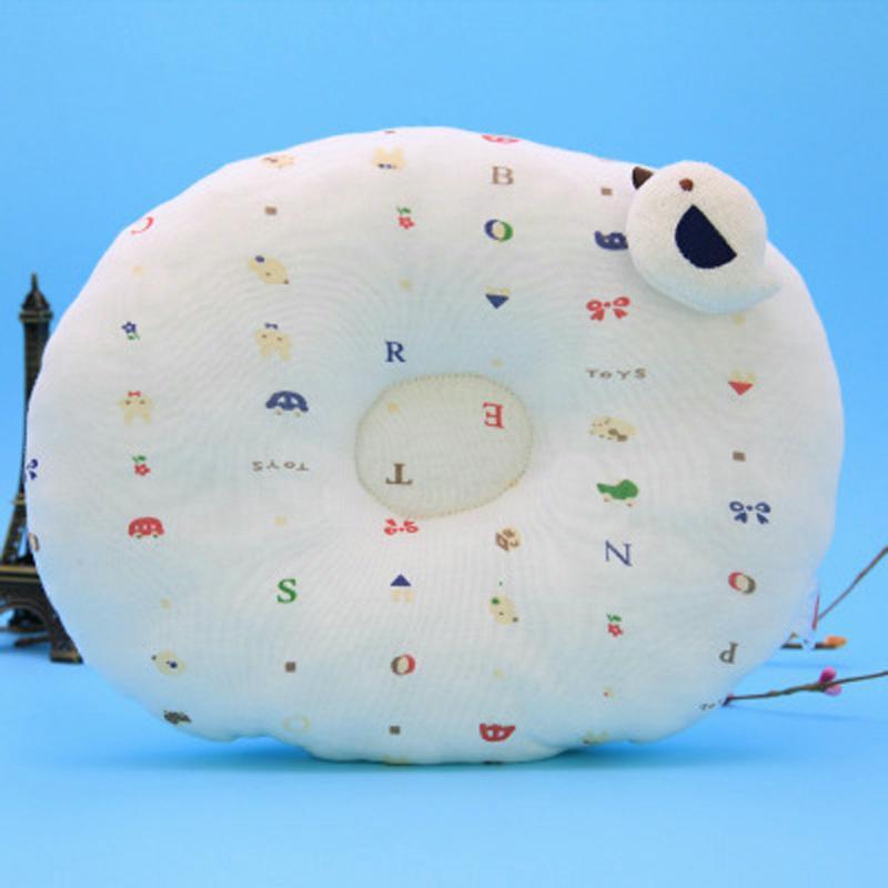 Round white pillow with colorful letters and tiny icons on a blue background. A small plush bird is attached to the top right of the pillow.