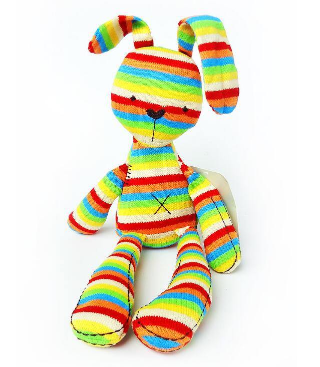 A colorful stuffed toy rabbit with alternating rainbow stripes, featuring floppy ears and stitched details, sits against a plain white background.